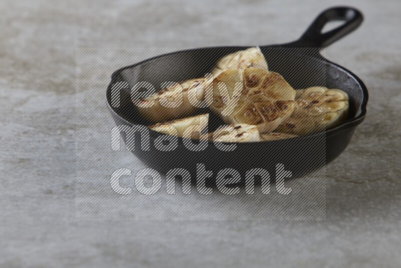half's roasted garlic in a black pan on a grey textured countertop