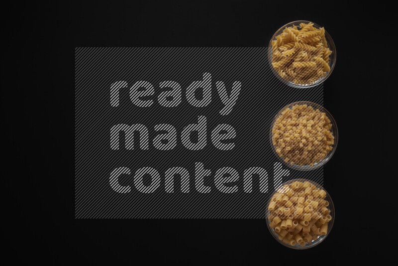 Different pasta types in 3 glass bowls on black background