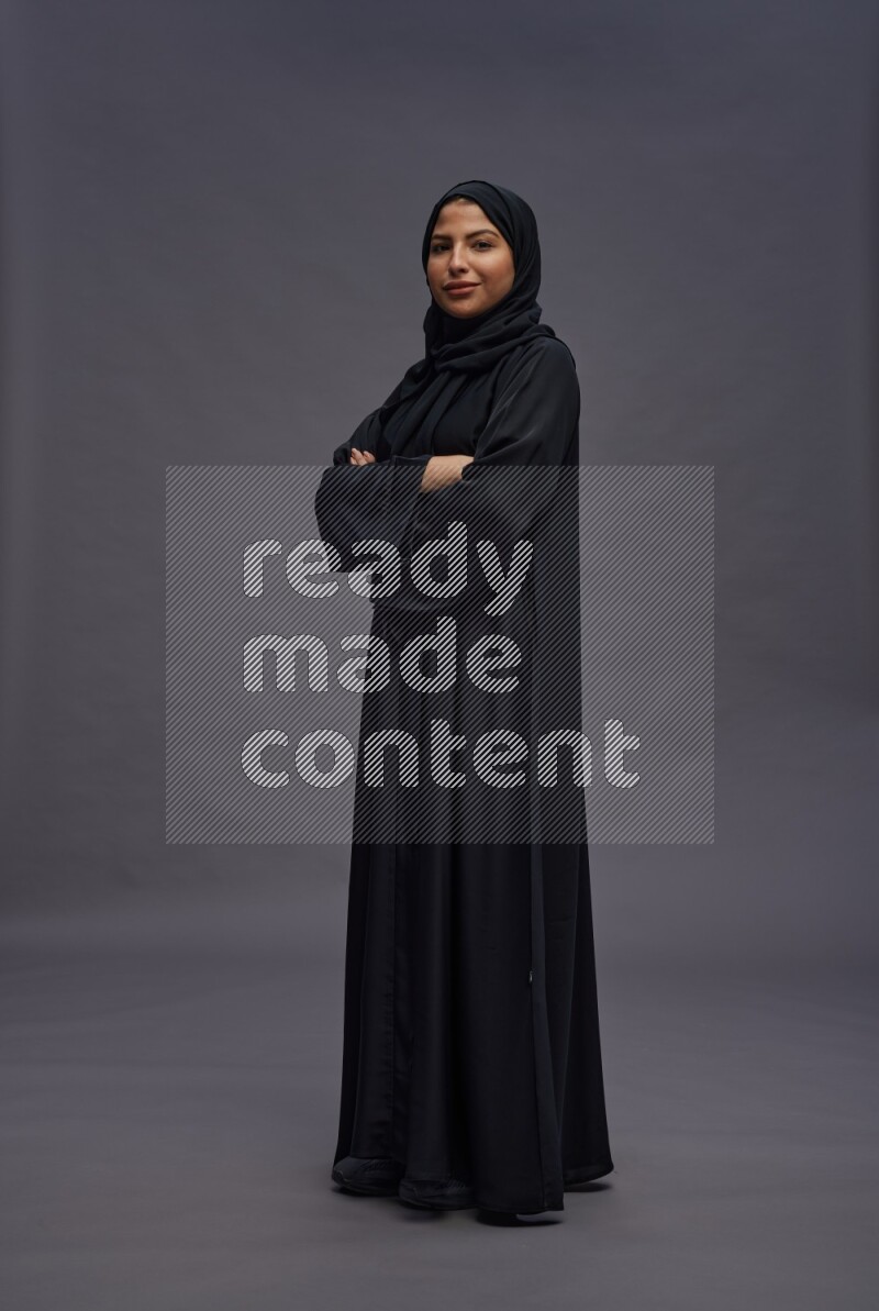 Saudi woman wearing Abaya standing with crossed arms on gray background