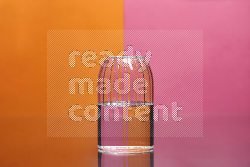 The image features a clear glassware filled with water, set against orange and pink background