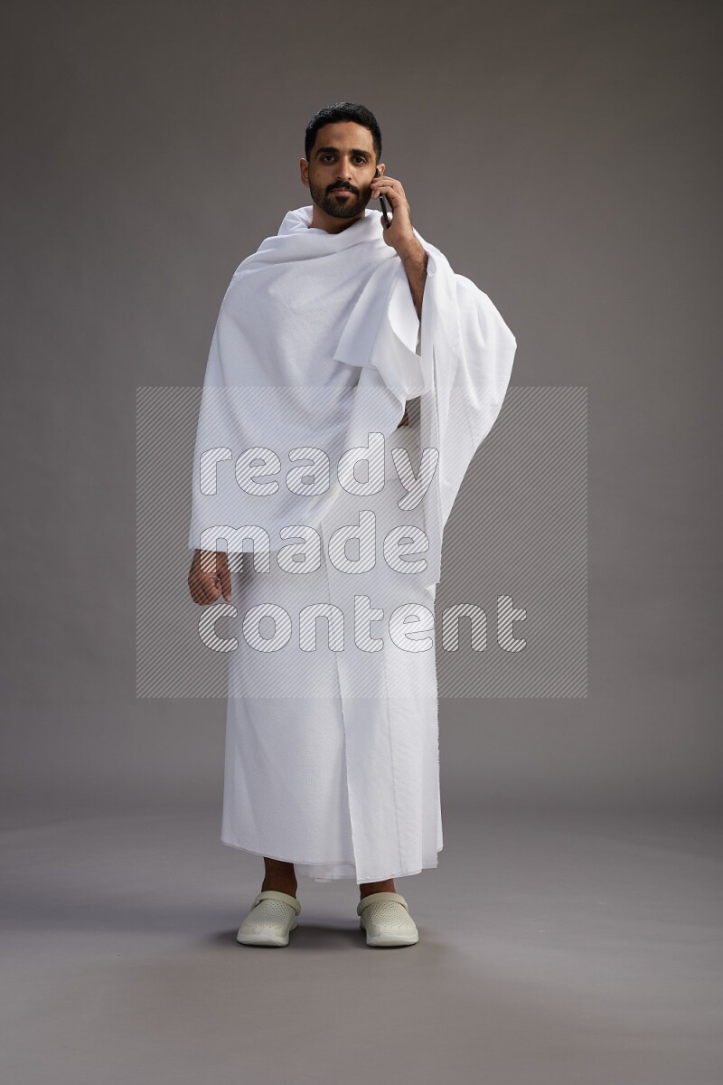 A man wearing Ehram Standing talking on phone on gray background