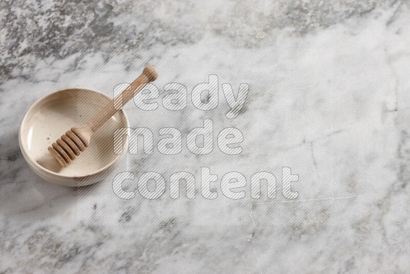 Beige pottery bowl with wooden honey dipper in it on grey marble background