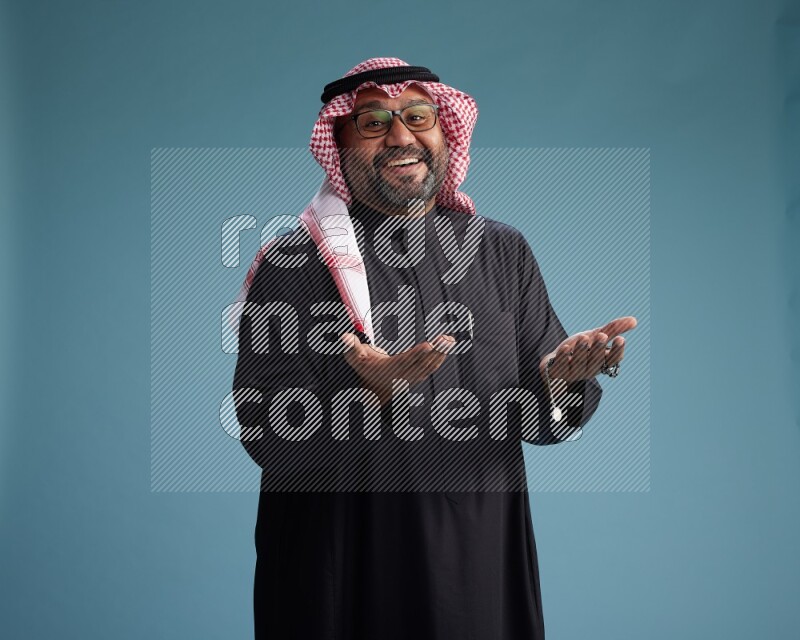 Saudi Man with shimag Standing Interacting with the camera on blue background