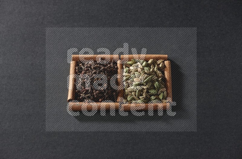 مربعان من أعواد القرفة ممتلئان بحبوب الهيل والقرنفل علي خلفية سوداء