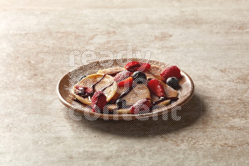 Five stacked mixed berries mini pancakes in a brown plate on beige background