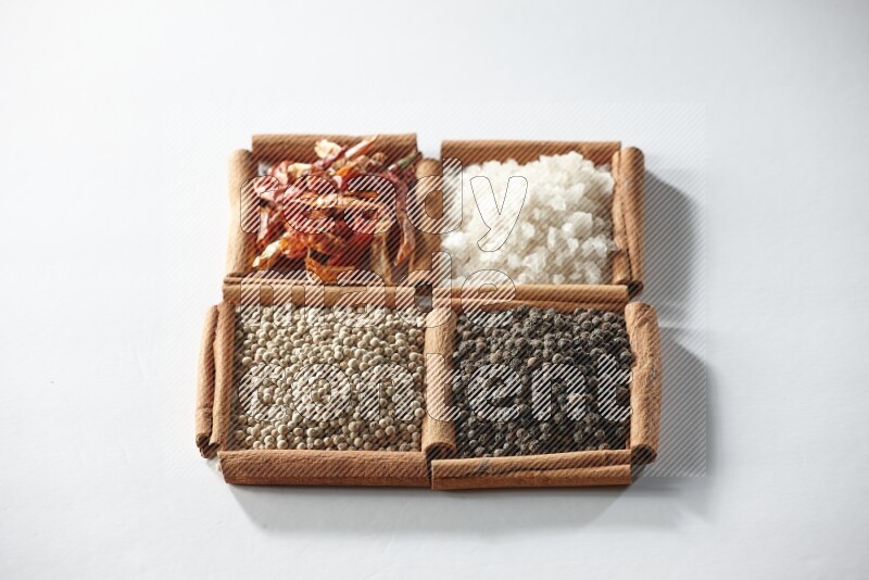 4 مربعات من أعواد القرفة ممتلئة بالفلفل الأحمر والملح والفلفل الأبيض والفلفل الأسود على أرضية بيضاء