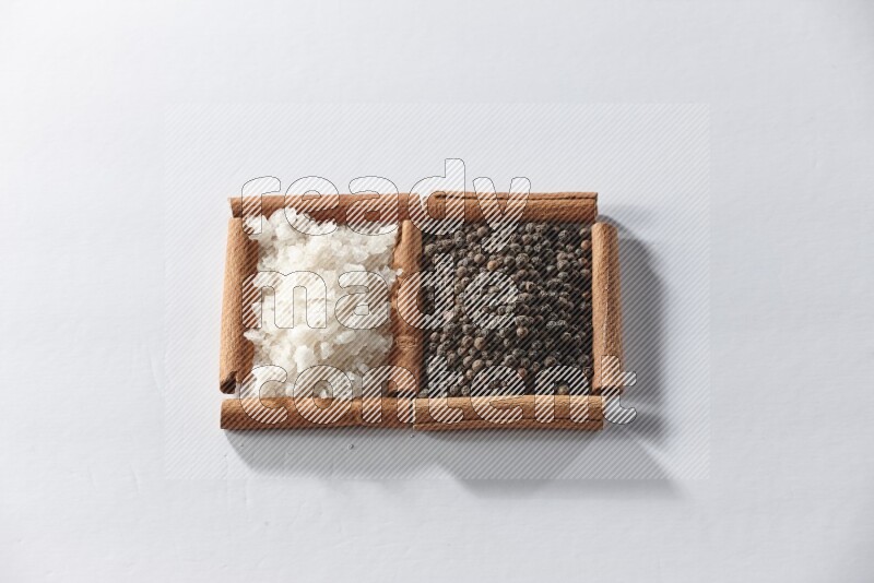 2 squares of cinnamon sticks full of black pepper and white salt on white flooring