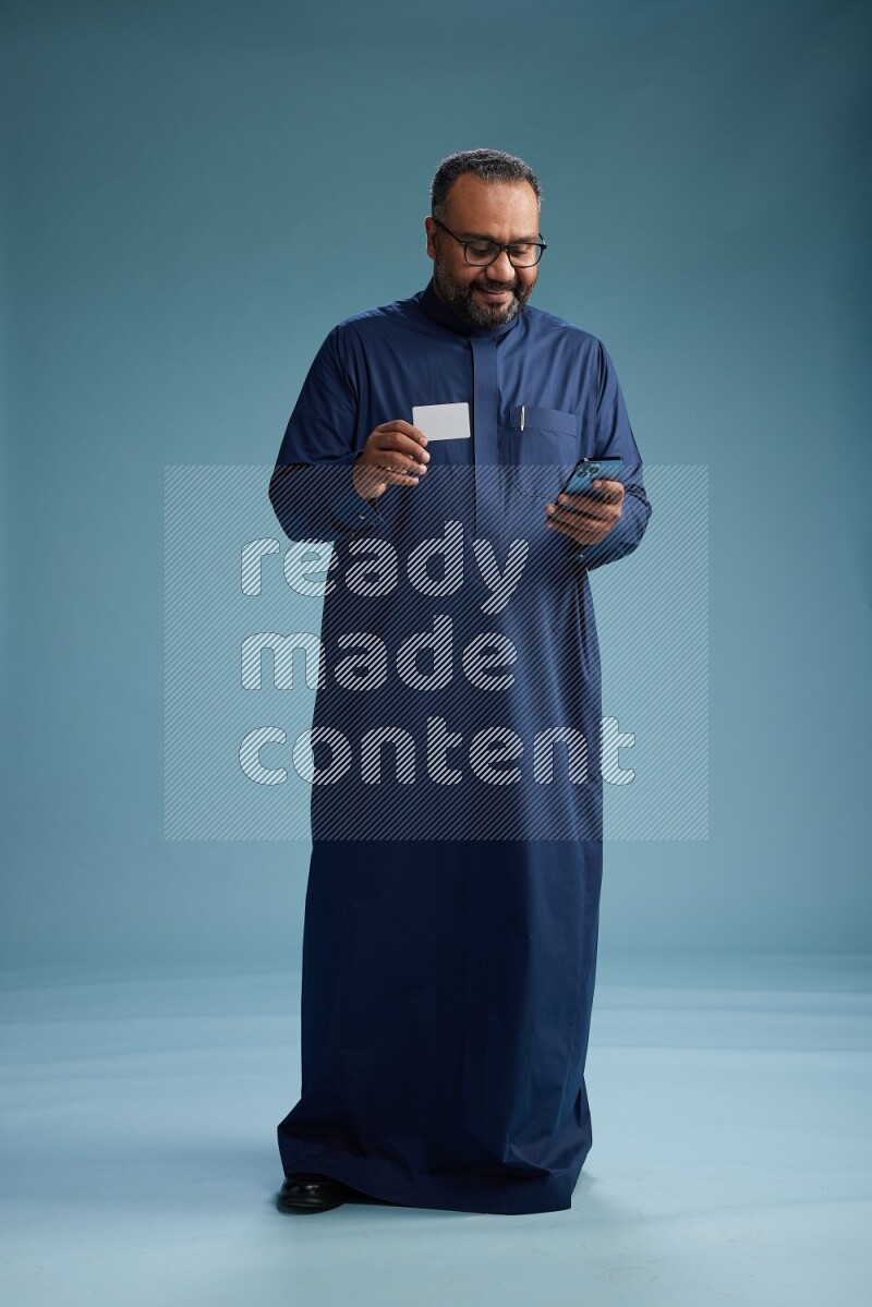 Saudi Man without shimag Standing holding ATM while talking on phone on blue background
