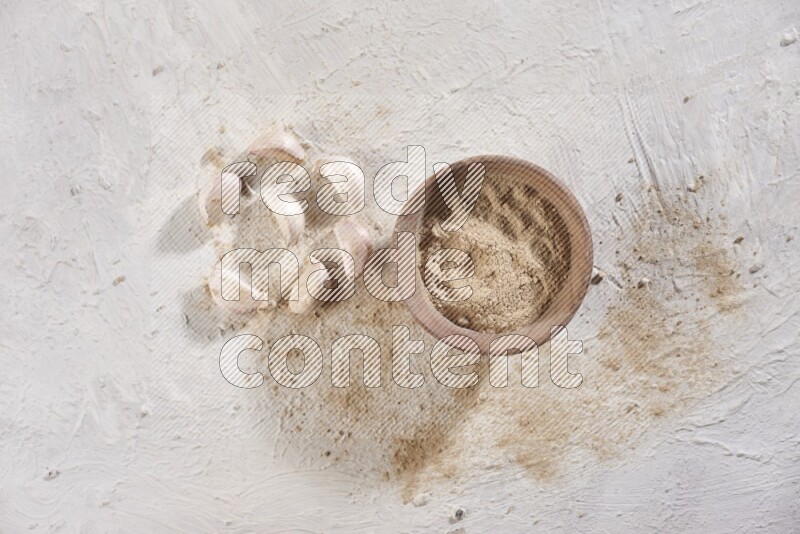 A wooden bowl full of garlic powder and beside it garlic cloves on a textured white flooring in different angles