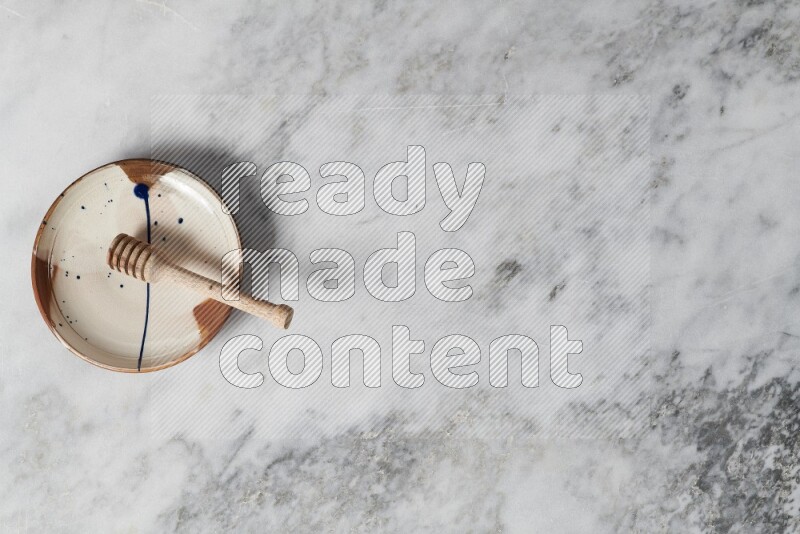 Multicolored pottery plate with wooden honey dipper in it on grey marble background