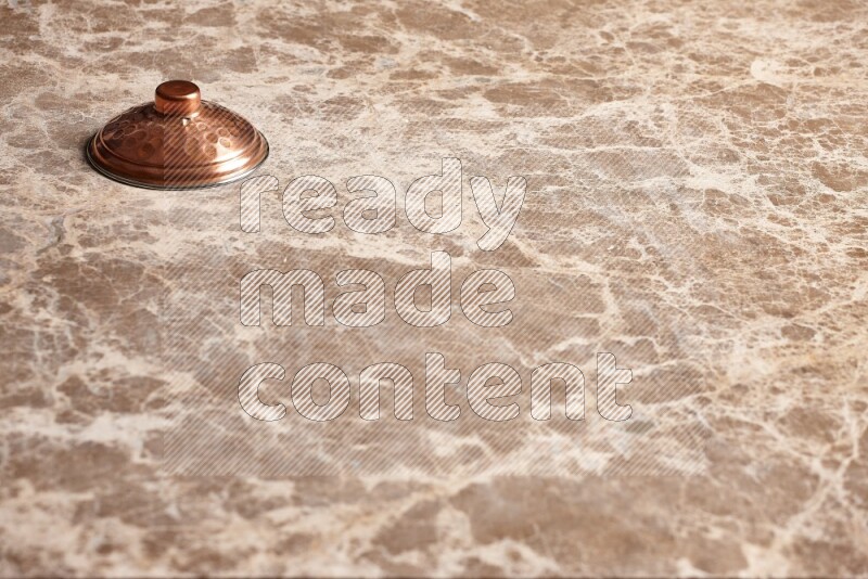A small copper pot lid on beige marble background