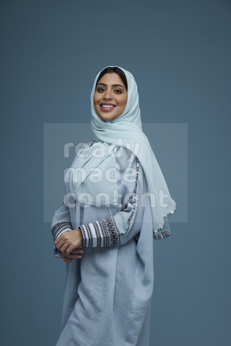 A woman posing in a blue background wearing a blue Abaya with hijab
