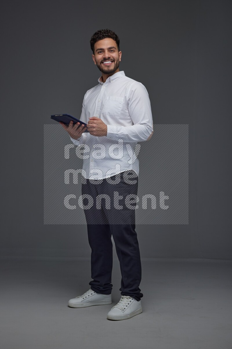 A man wearing smart casual standing and using his tablet eye level on a gray background