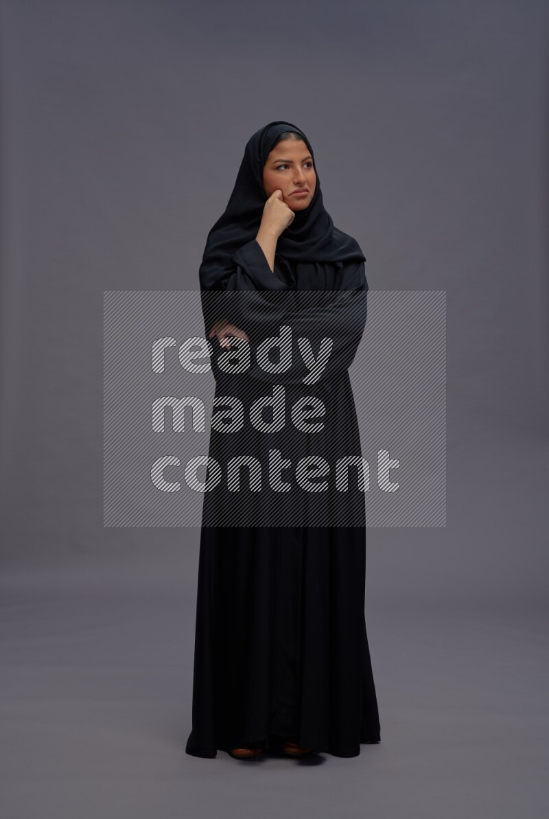 Saudi woman wearing Abaya standing interacting with the camera on gray background