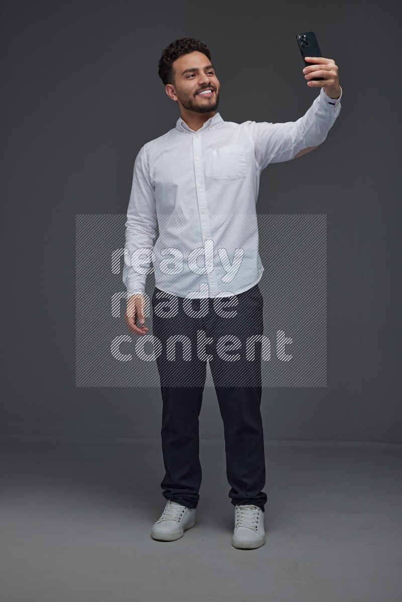 A man wearing smart casual and taking selfie with his phone eye level on a gray background
