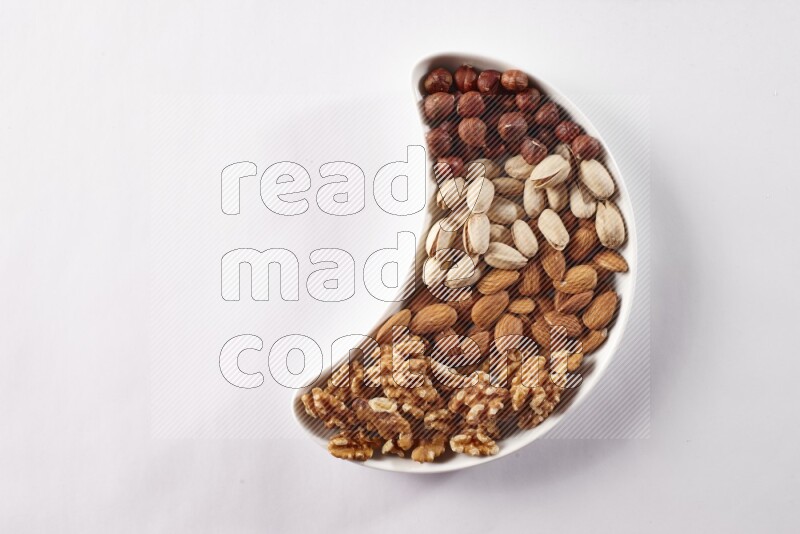 Mixed nuts in a crescent pottery plate on white background