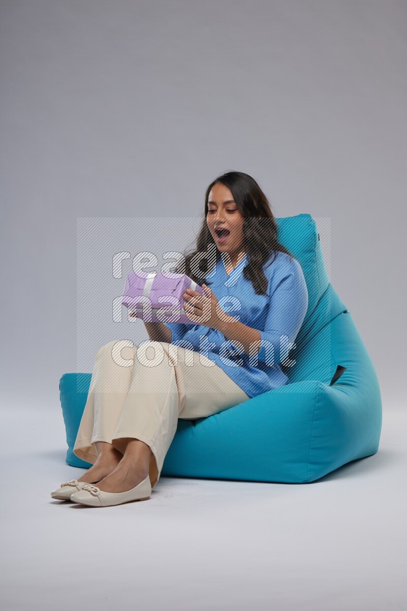 A woman sitting on a blue beanbag and holding a gift