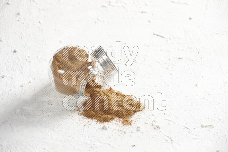Flipped glass jar full of cinnamon powder on a textured white background