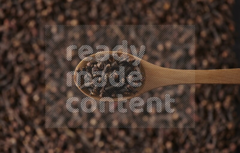 A wooden spoon full of cloves on cloves background and black flooring