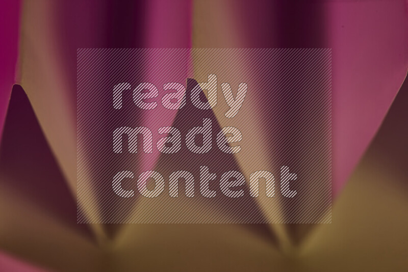 A close-up abstract image showing sharp geometric paper folds in pink gradients and warm tones