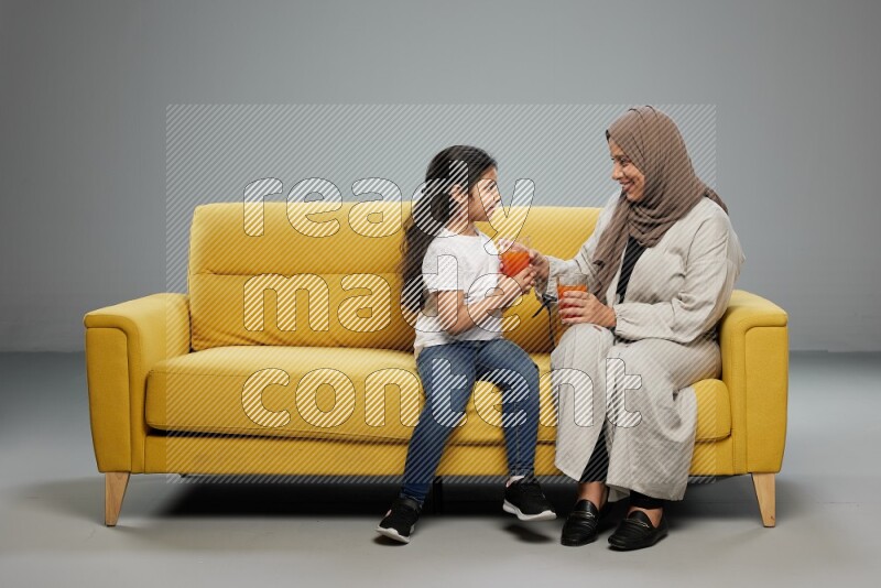 Mom and daughter sitting drinking juice on gray background