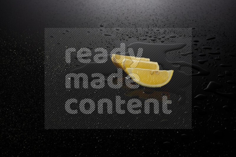 Lemon wedges with water drops, and droplets on black background