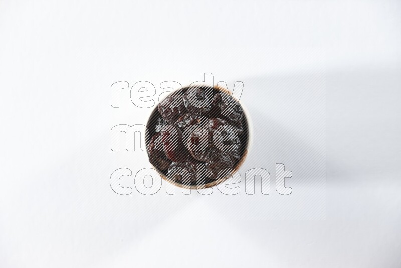 A beige ceramic bowl full of dried plums on a white background in different angles