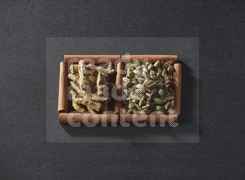 مربعان من أعواد القرفة ممتلئان بحبوب الهيل وأصابع الكركم علي خلفية سوداء