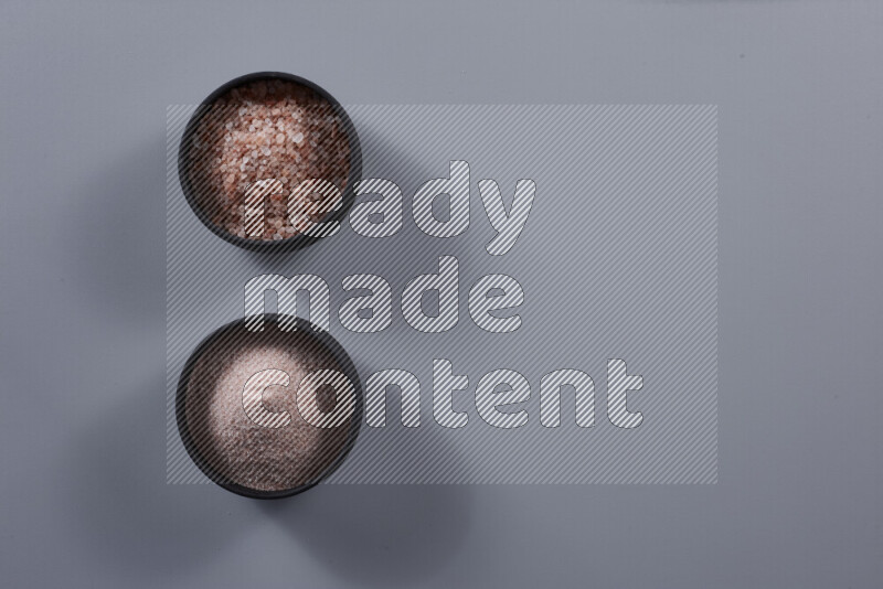 2 وعاء فخاري احدهمها ممتلئ بملح الهيمالايا الناعم والأخر بملح الهيمالايا الخشن على خلفية رمادية