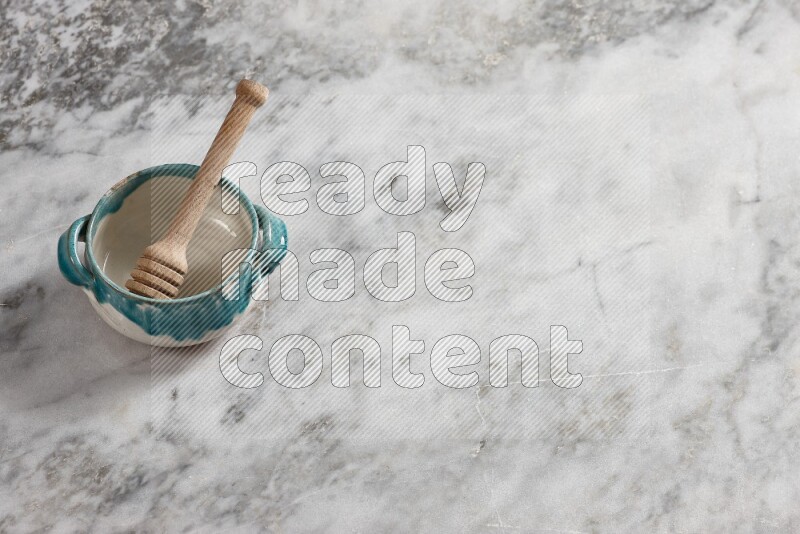 Multicolored pottery bowl with wooden honey dipper in it on grey marble background