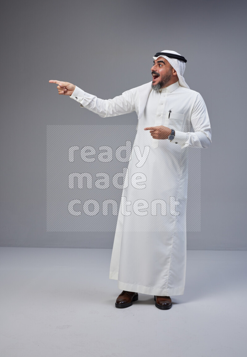 Saudi man Wearing Thob and white Shomag standing interacting with the camera on Gray background