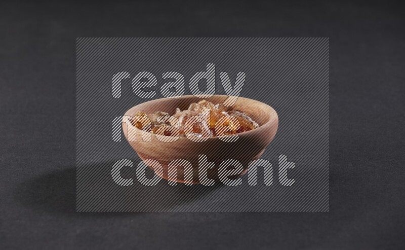 A wooden bowl full of gum arabic on a black flooring