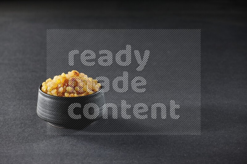 A black pottery bowl full of raisins on a black background in different angles