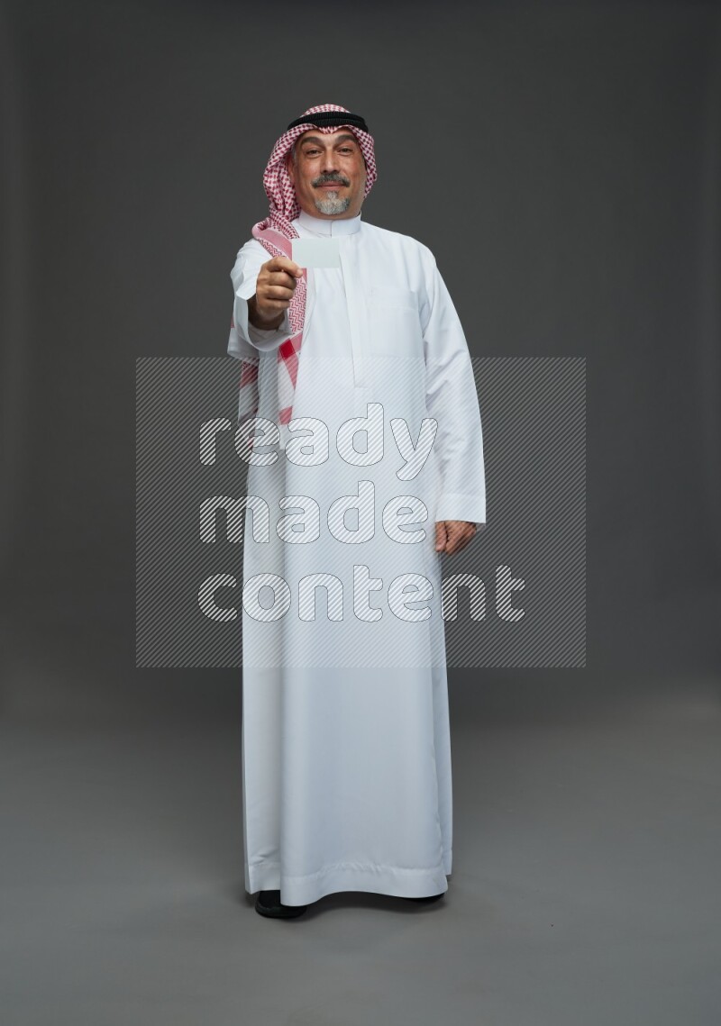 Saudi man with shomag Standing holding ATM card on gray background