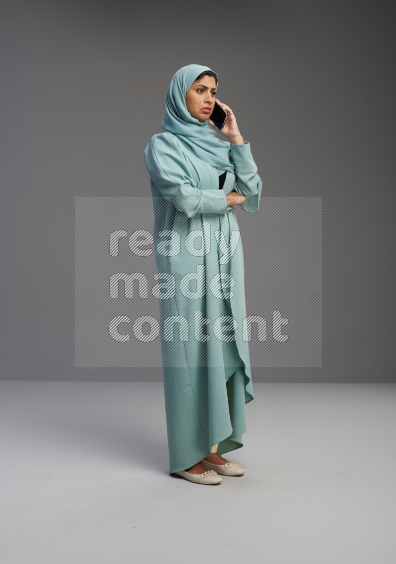 Saudi Woman wearing Abaya standing talking on phone on Gray background