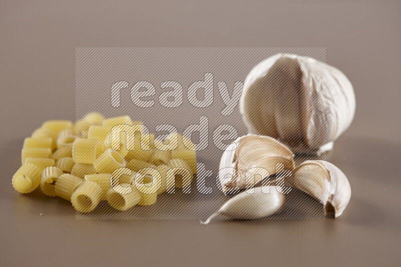 Raw pasta with different ingredients such as cherry tomatoes, garlic, onions, red chilis, black pepper, white pepper, bay laurel leaves, rosemary and cardamom on beige background