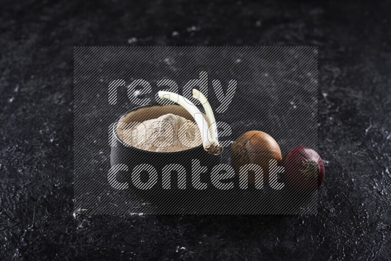 A black pottery bowl full of onion powder on black background