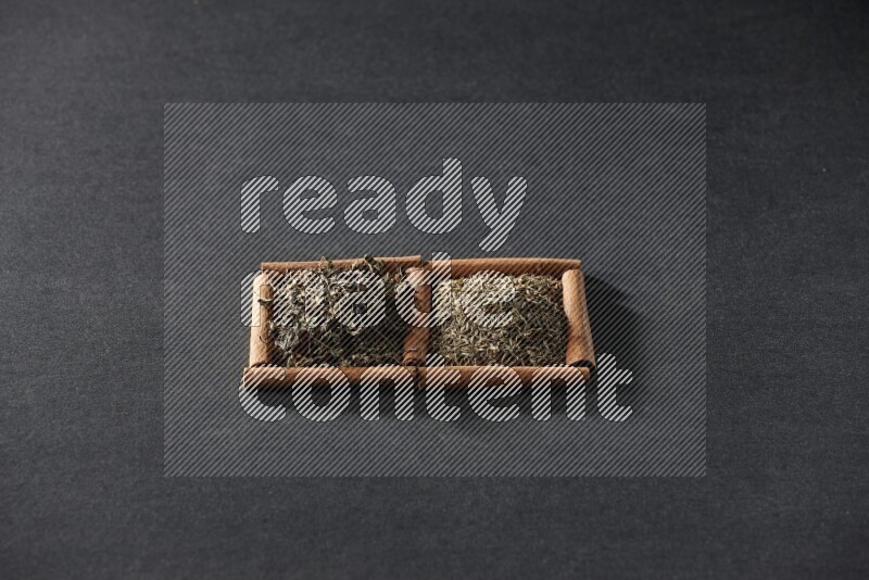 2 squares of cinnamon sticks full of cumin and dried basil on black flooring