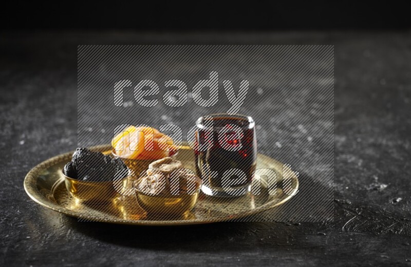 Dried fruits in metal bowls with tamarind on a tray in dark setup