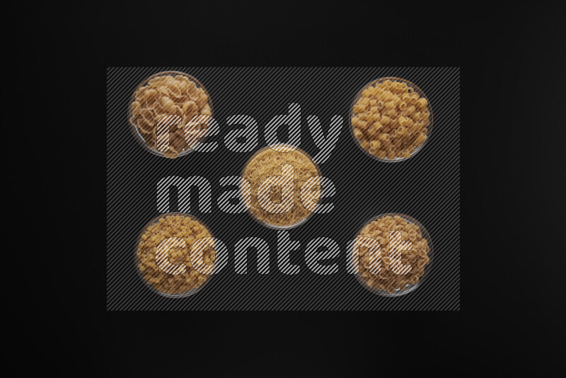 Different pasta types in 5 glass bowls on black background