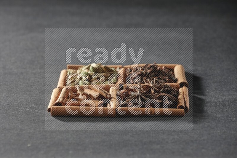 4 مربعات من عيدان القرفة ممتلئة بقطع القرفة وحبوب الهيل والقرنفل اليانسون النجمي على أرضية سوداء