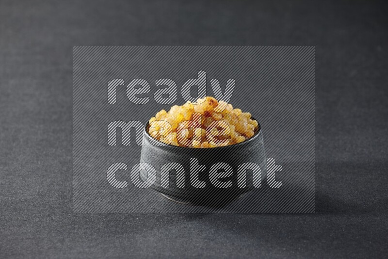 A black pottery bowl full of raisins on a black background in different angles