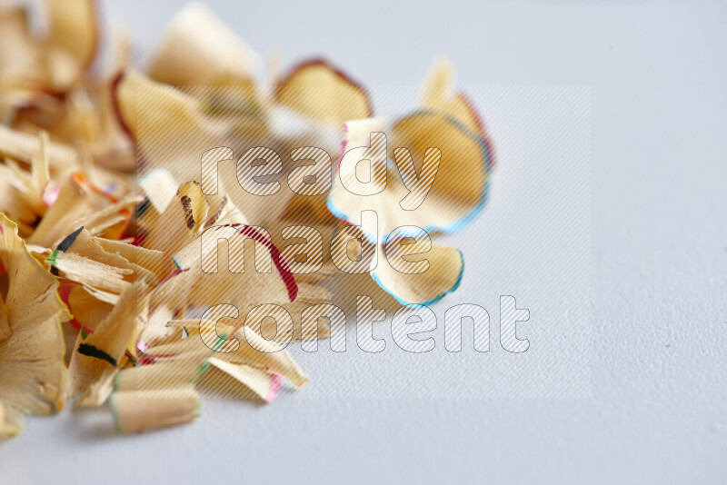 A close-up showing a small pile of pencil shavings with varied color edges on grey background