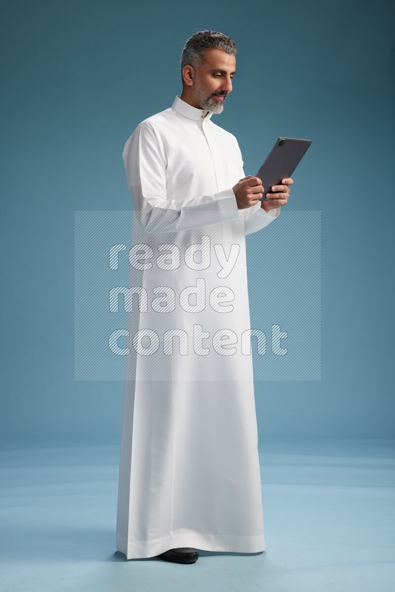 Saudi man waring thob with tablet on blue background