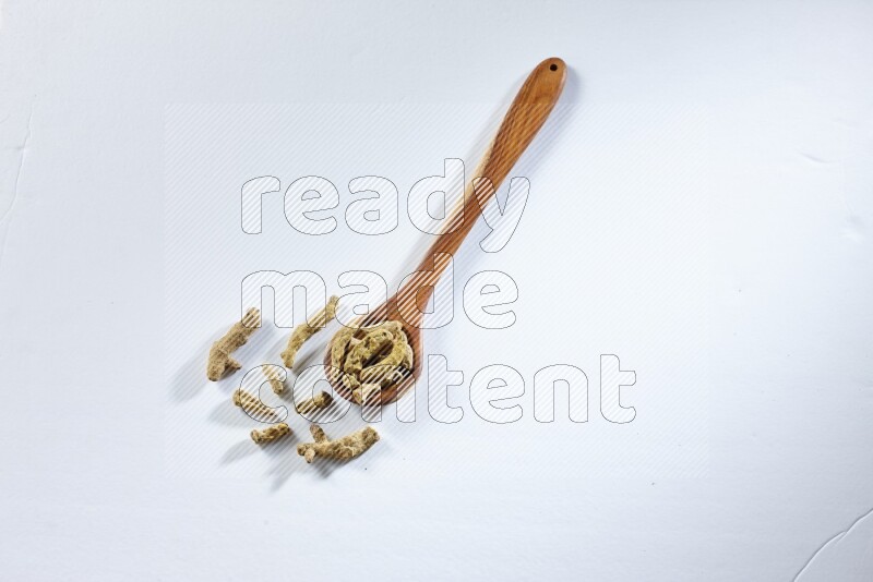 A wooden ladle full of dried turmeric fingers on white flooring
