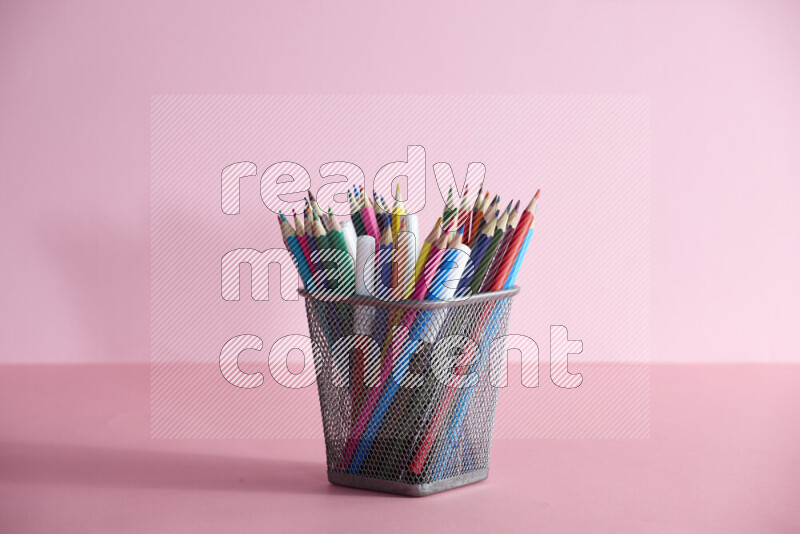 Pens, pencils and other different school supplies in a metal pen holder on rose background