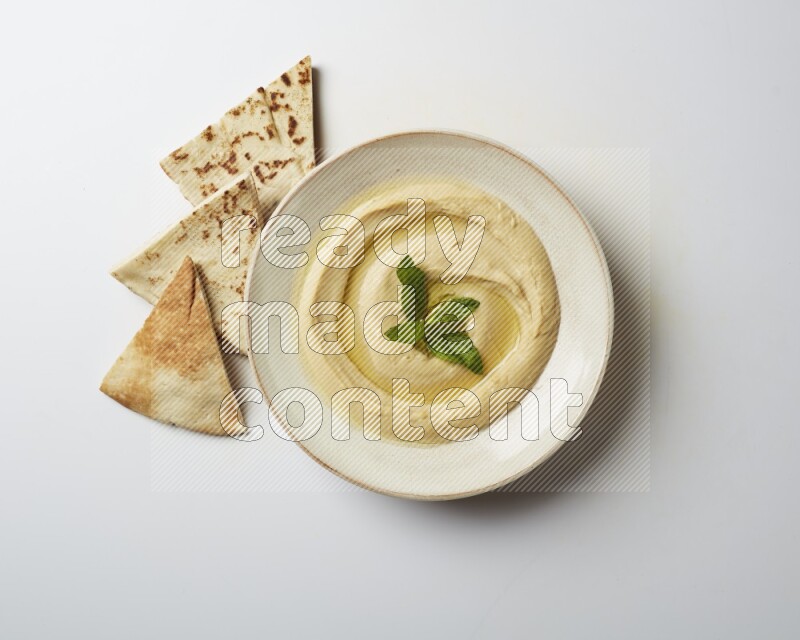 Hummus in a pottry plate garnished with mint  on a white background