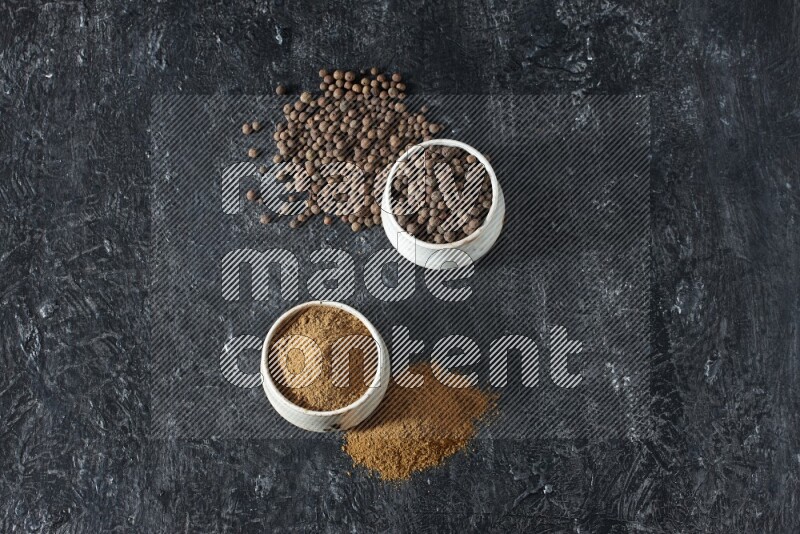 2 beige bowls, one full of allspice powder and the other full of whole balls and both spread on a textured black flooring