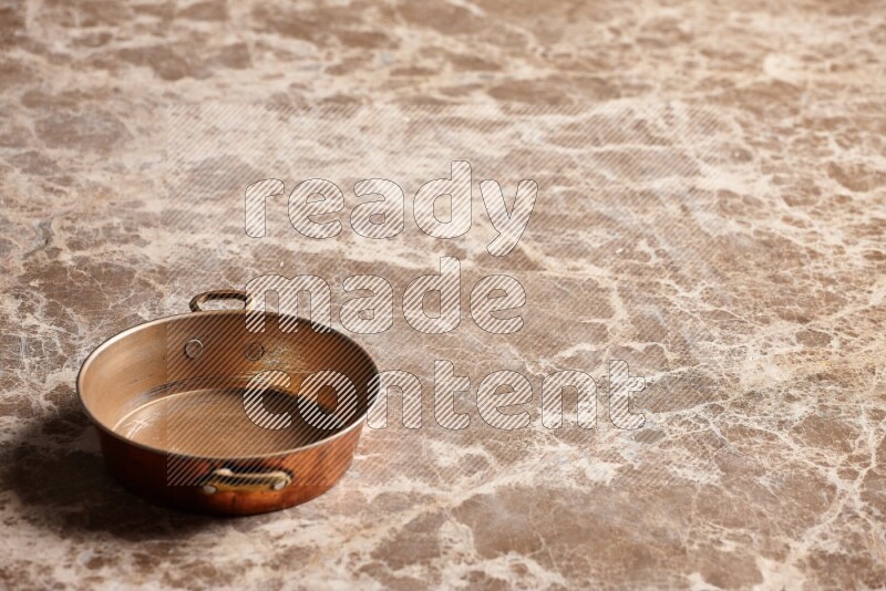A small copper pan on beige marble background