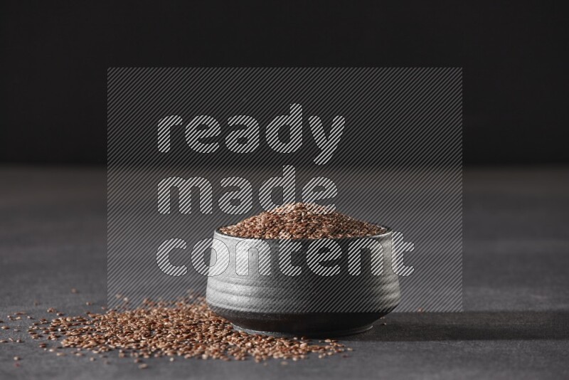 وعاء فخاري أسود ممتلئ بحبوب بذر الكتان محاط بالبذور على أرضية سوداء